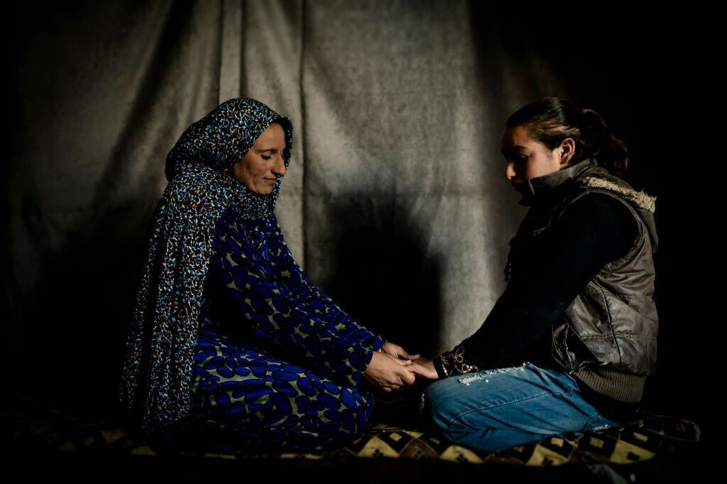 Amal and Abir, a mother and daughter, holding hands inside their tent in the Syrian refugee settlement