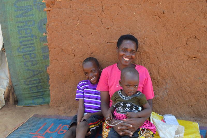 Elisa, a little boy in the Uganda settlement, sitting with his mother and younger brother