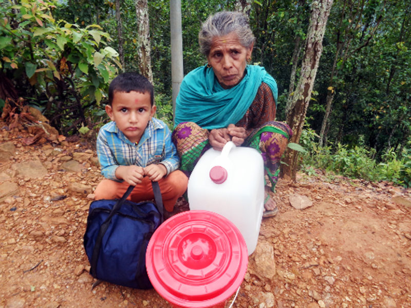 Indra and her grandson Saurav, crouching on the ground in Chainpur holding hygiene kits they distribute to their community