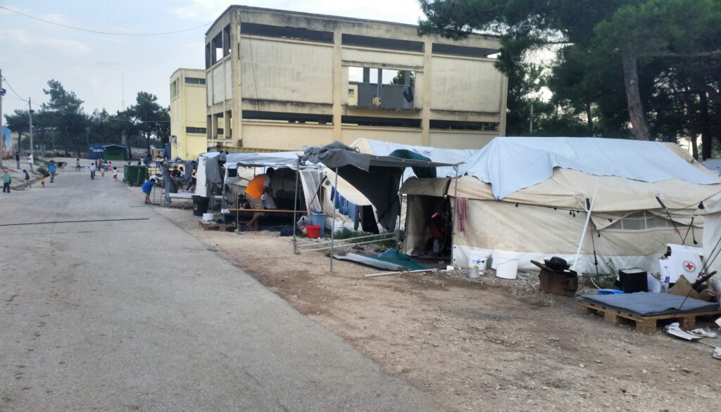 A camp in Diavata, Greece, where tents are pitched along a dirt road and people live in close quarters 