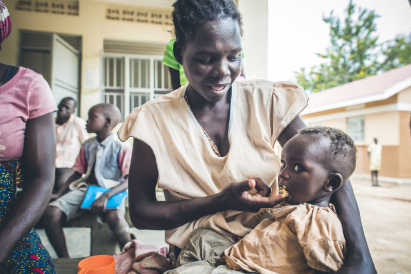 A smiling refugee woman feeding supplemental food to her baby, Brenda