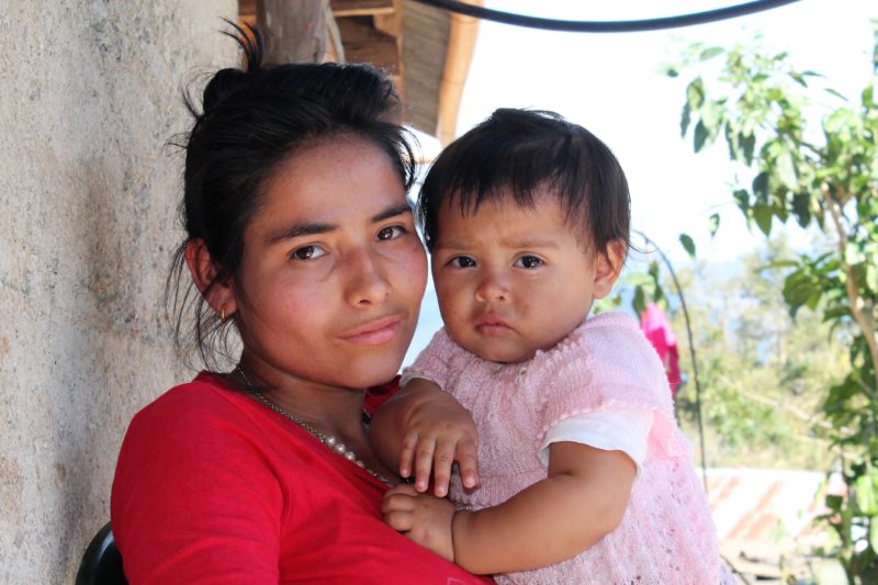A smiling woman from Guatemala holding her young daughter