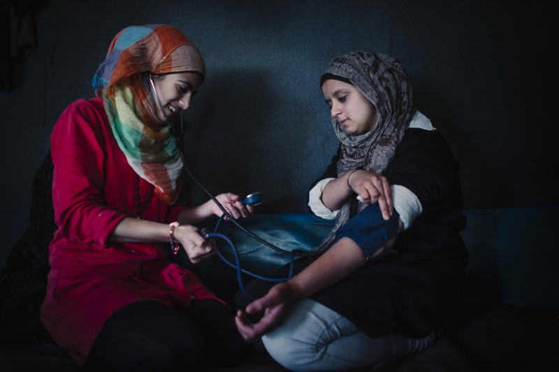 A community health worker take the blood pressure of another refugee woman