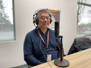 Dr. Marc Iwahiro with headphones on sits in front of a microphone 