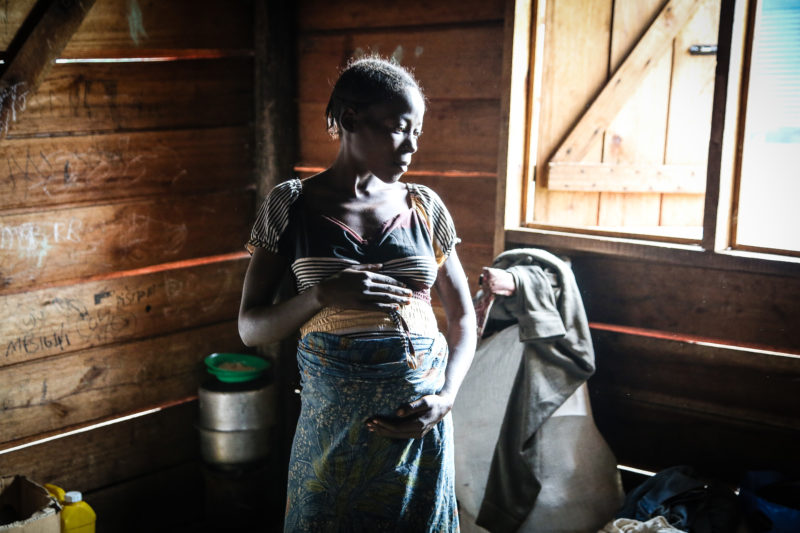 Mama Myombi cradling her pregnant belly in a refugee shelter