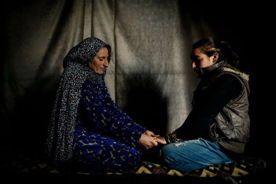 Amal and Abir, a mother and daughter, holding hands inside their tent in the Syrian refugee settlement