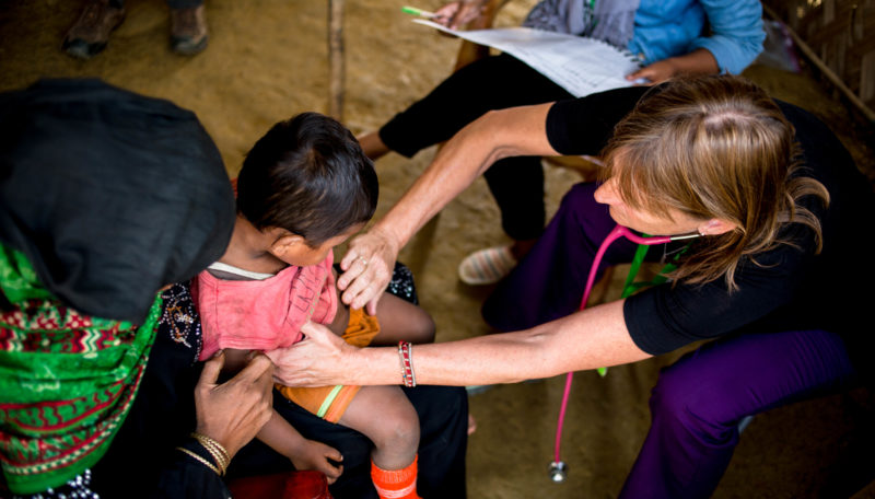 A volunteer abroad providing screening for injuries, illnesses, and malnutrition to a young refugee entering a camp