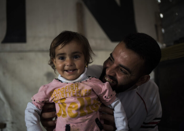 A Syrian refugee father and daughter smiling, find a moment of joy.