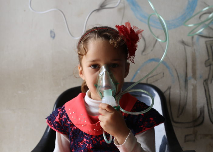Young Syrian refugee with an oxygen mask provides support against deadly asthma attacks.