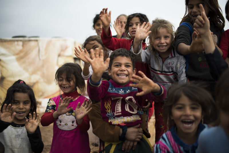 Smiling refugee children waving at the camera in a refugee camp