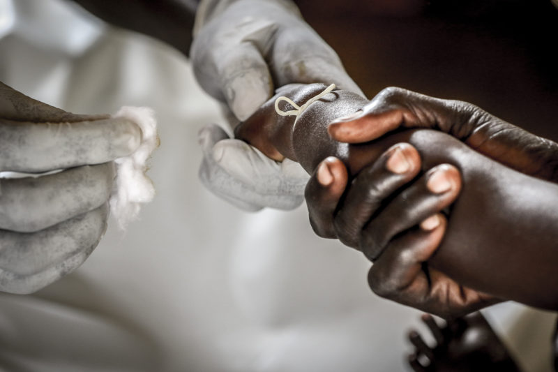 A refugee child extending his arm to the medical volunteer hands to a dress a wound