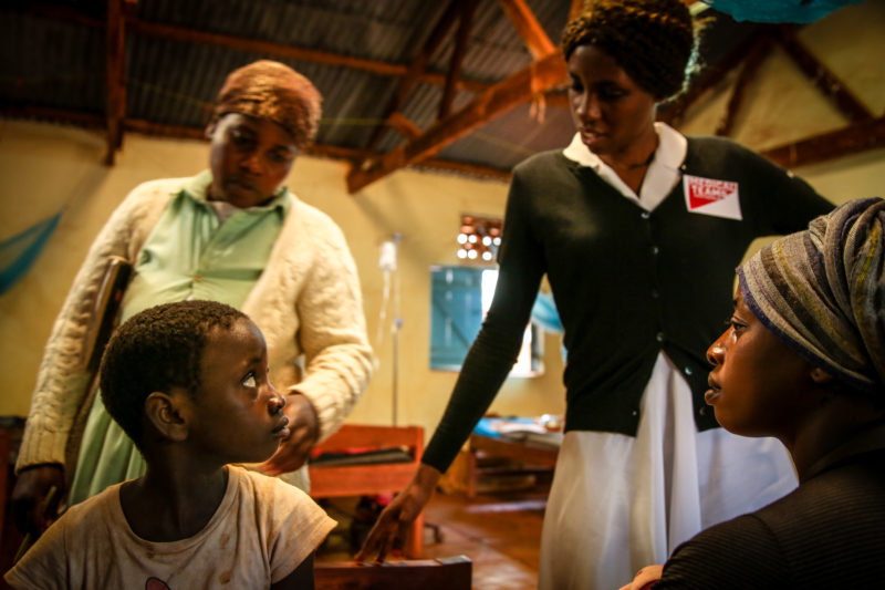 Two Community Health Workers checking in on Kentia in the hospital wing of the Medical Team-supported hospital in Tanzania