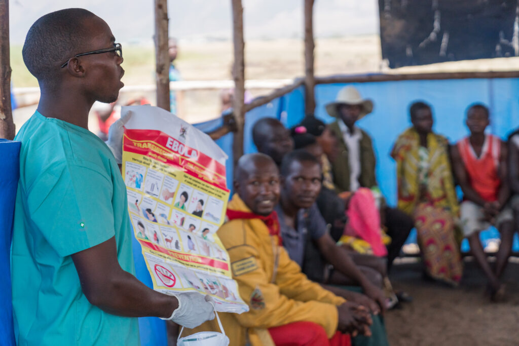 A man wearing scrubs instructs a crowd on the symptoms of Ebola 