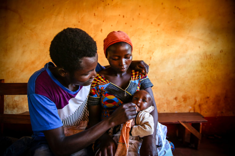 Fidel, a refugee father, wiping the mouth of his newborn girl after eating supplemental foods to aid her malnutrition