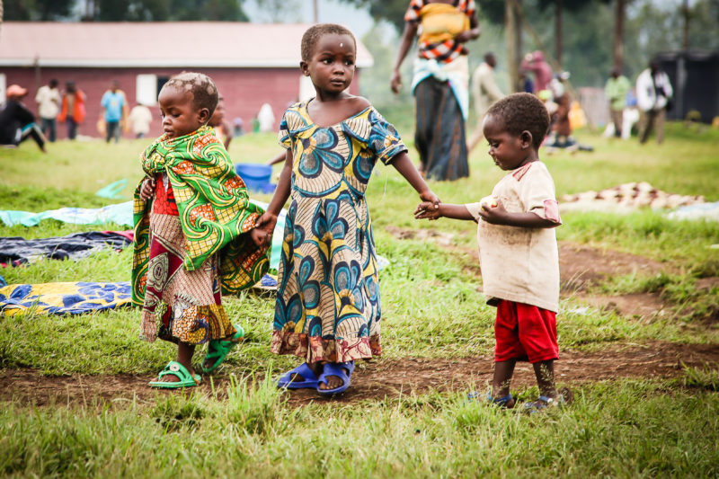 Three Uganda refugee children holding hands in a field of the health centers
