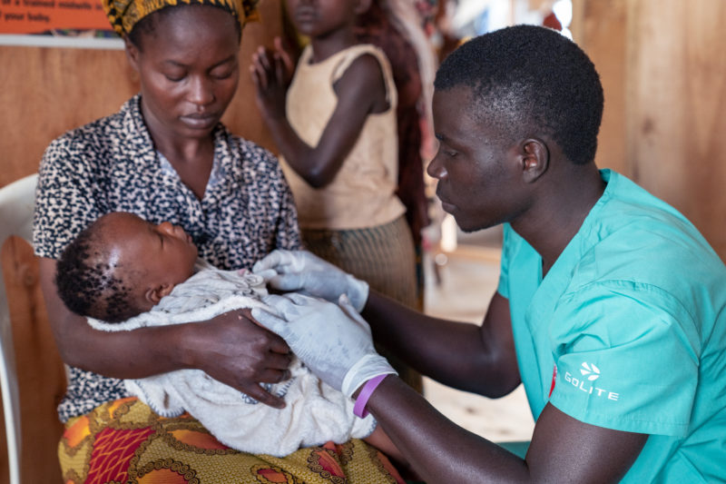 •A Uganda refugee and community health worker giving medical care to a baby held by its mother