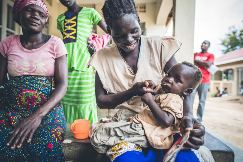 A smiling refugee woman feeding supplemental food to her baby, Brenda