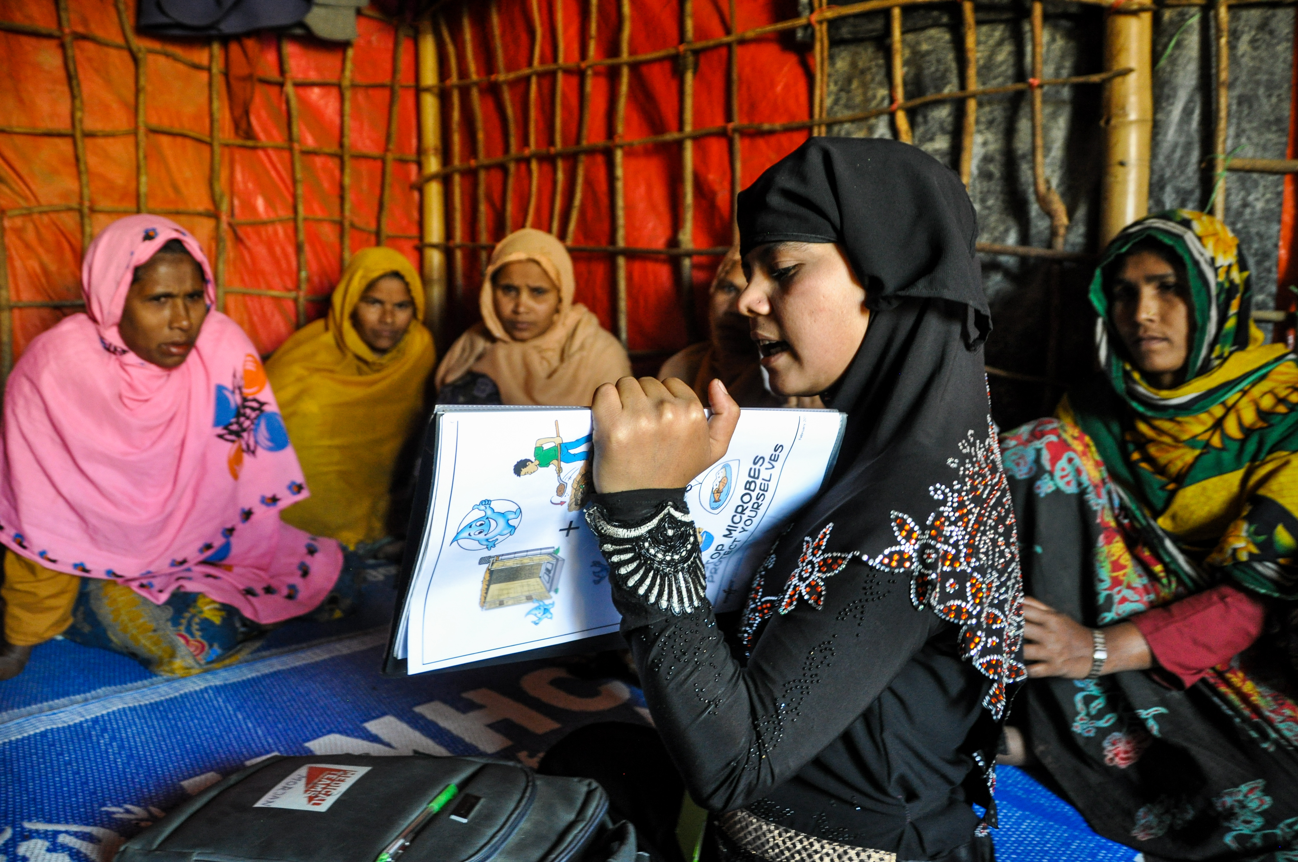 Morjan, a Rohingya refugee and Community Health Worker, shares health messages with refugee women in a camp tent