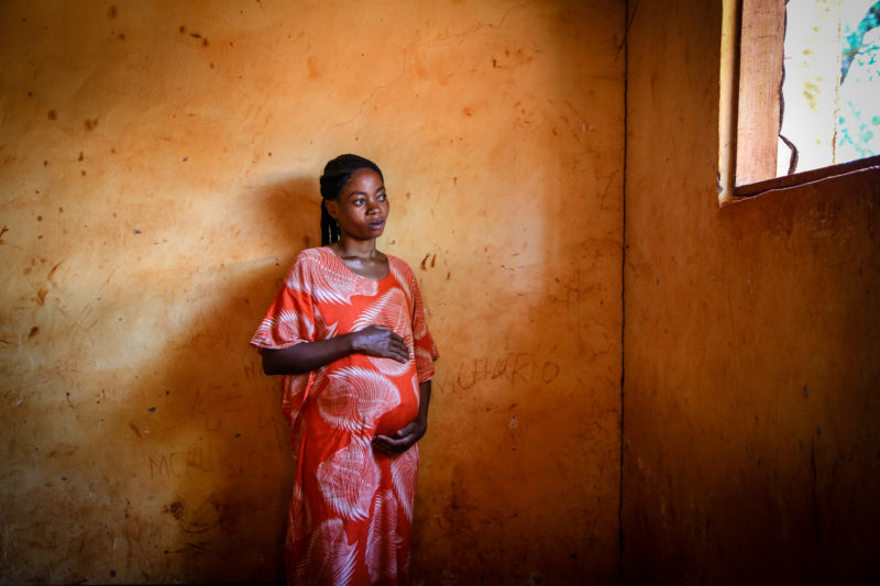 Pregnant refugee woman in an orange dress cradles her belly