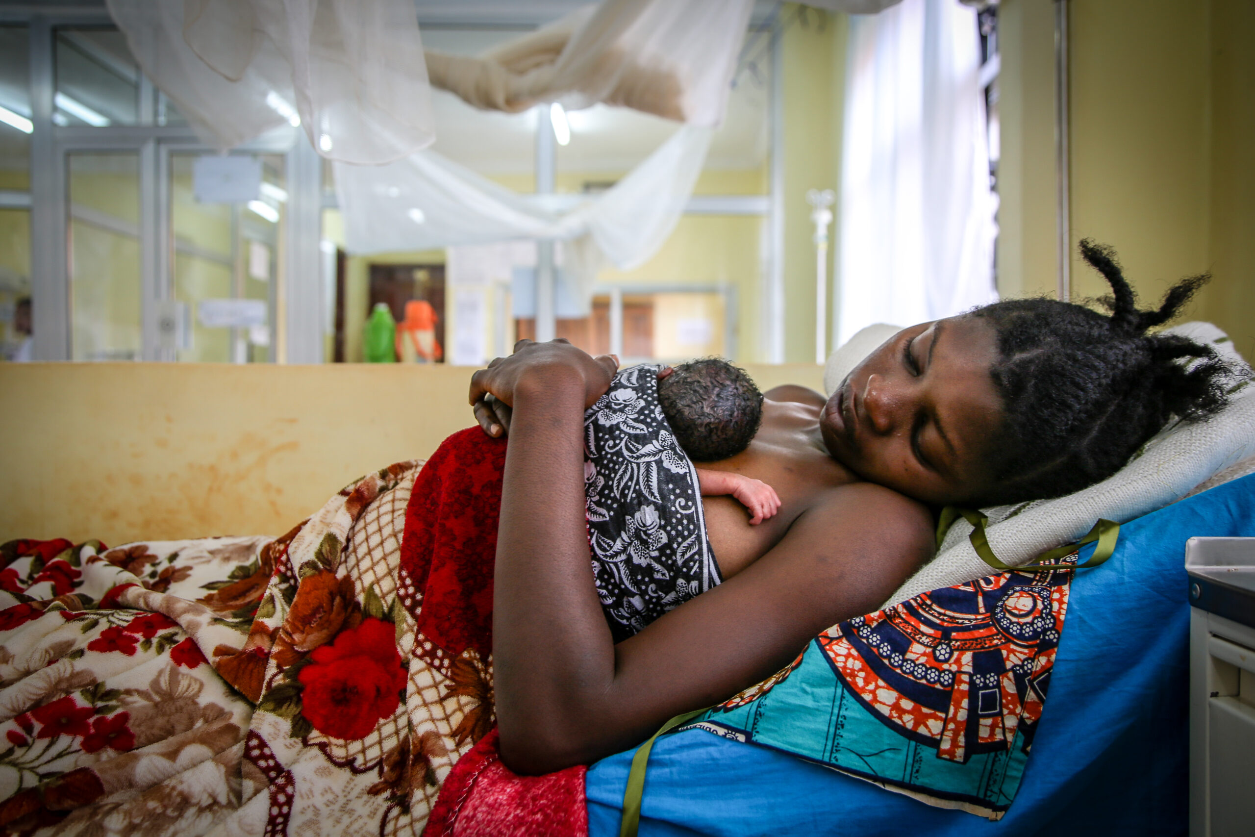 mother rests in bed with newborn baby on her chest