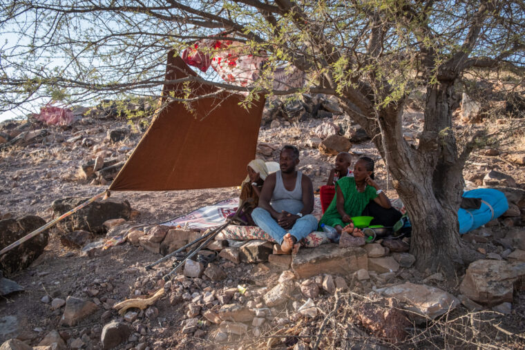 A family sits under a makeshift tent and tree, Ethiopian refugees in transit. Photo by Joost Bastmeijer.