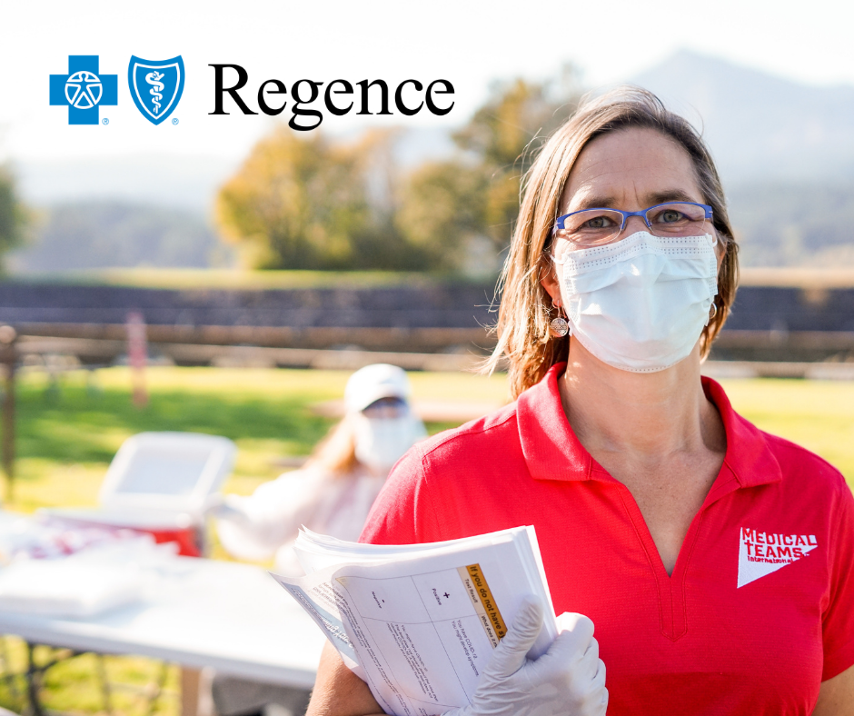 A woman wearing a bright red polo shirt and face masks holds paperwork and stands outside of an outdoor COVID-19 testing clinic in Cascade Locks, Oregon.