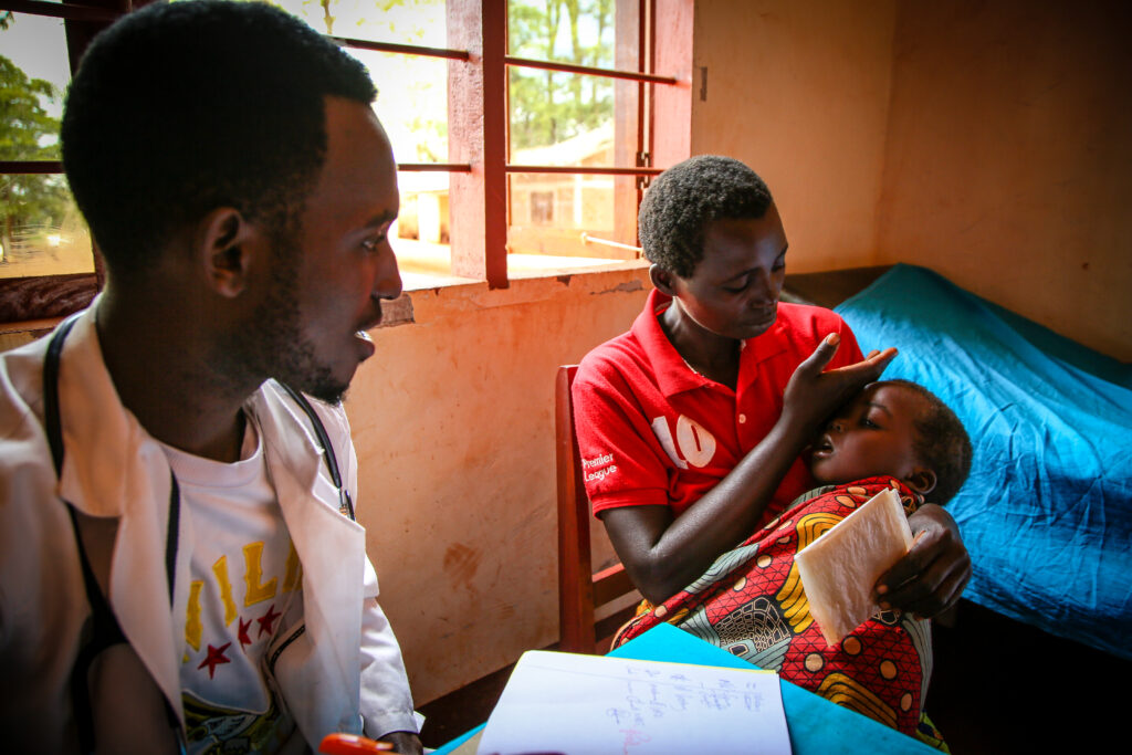 a mother holds her sick child while speaking with a doctor