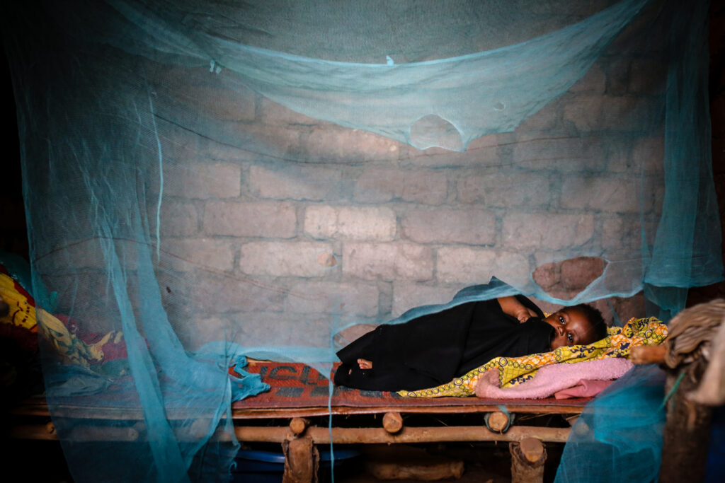 A baby lays under a mosquito net with large holes in it.