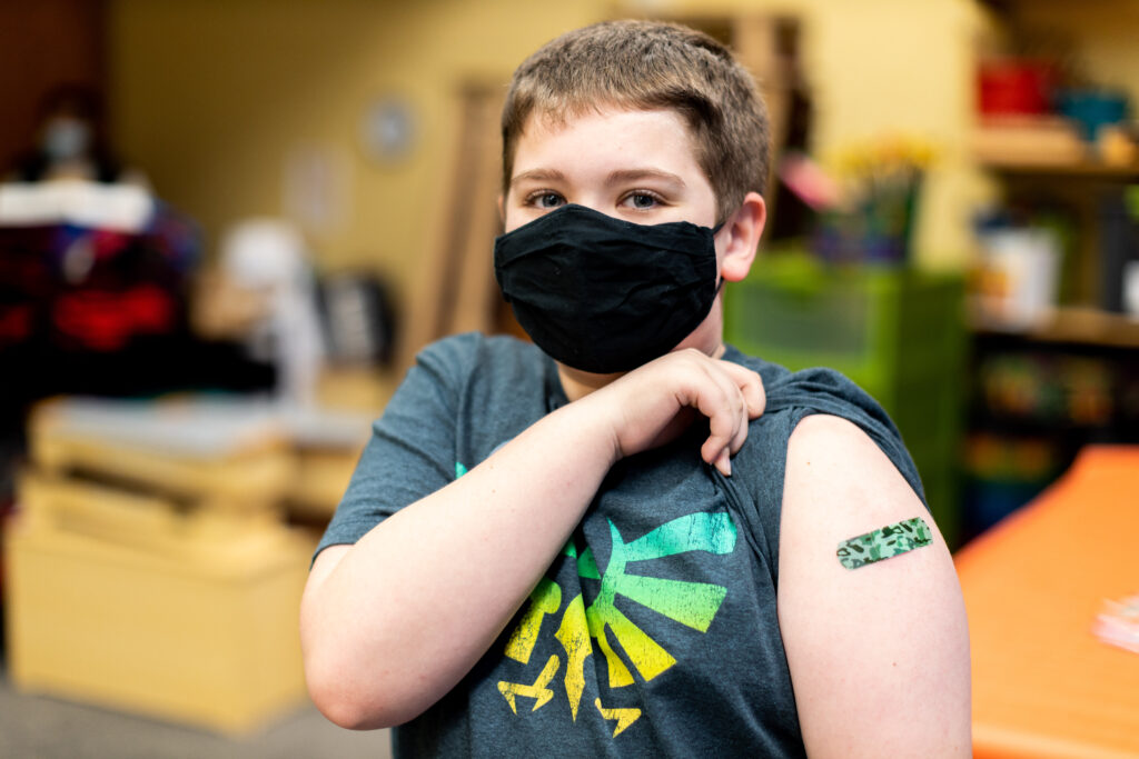 young boy lifting his sleeve to show a band-aid on his arm