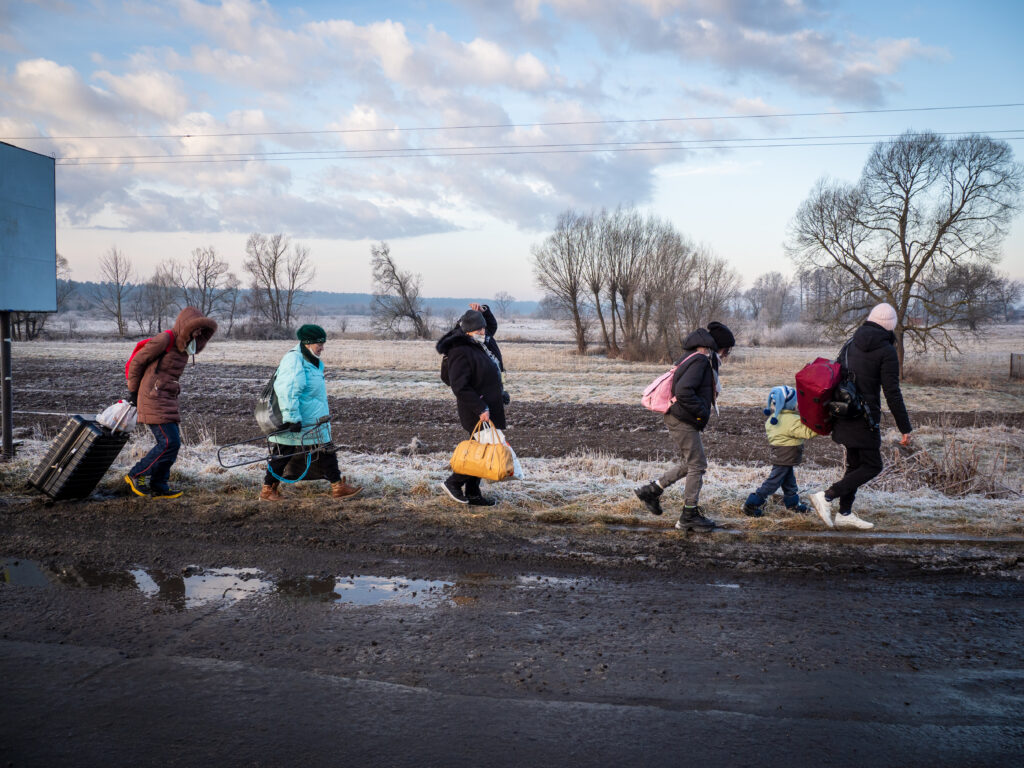 People with bags walking single file along road