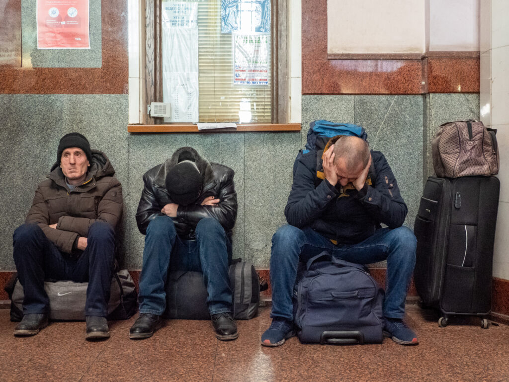 Three men sit on suitcases waiting