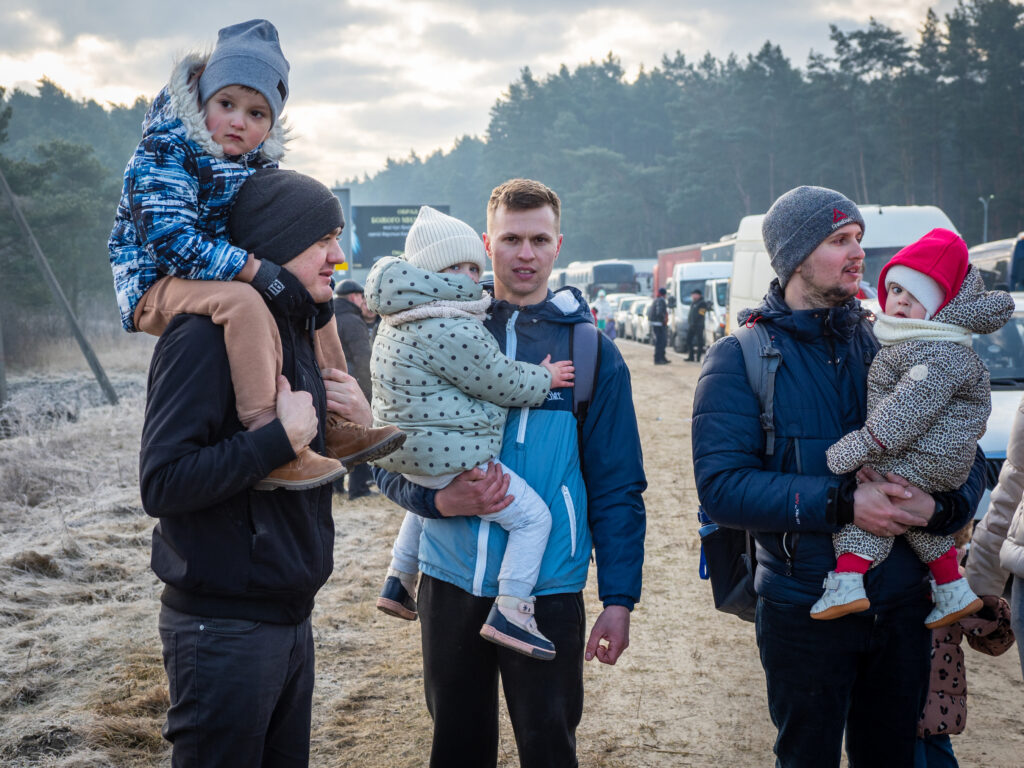 Three men carry their small children along a road