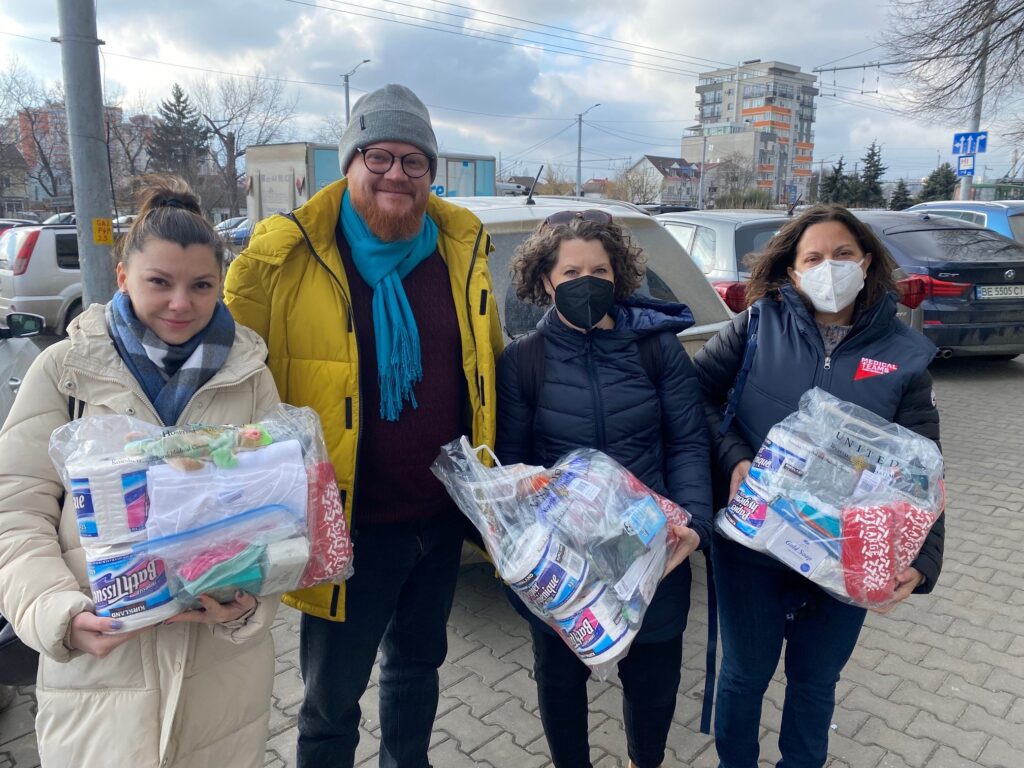 four people holding plastic bags filled with various hygiene items like toilet paper, toothbrushes, soap, etc. -- supporting the Ukraine crisis