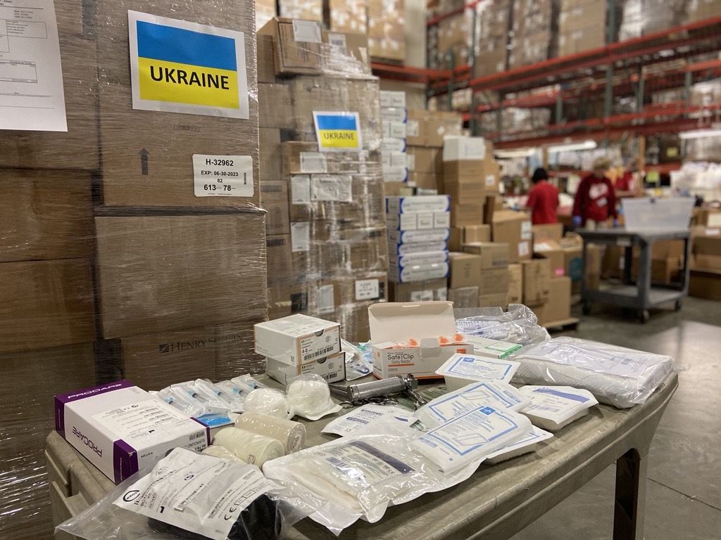 medical supplies laid out on table with pallets of boxes labeled "Ukraine" in background, supporting the Ukraine crisis