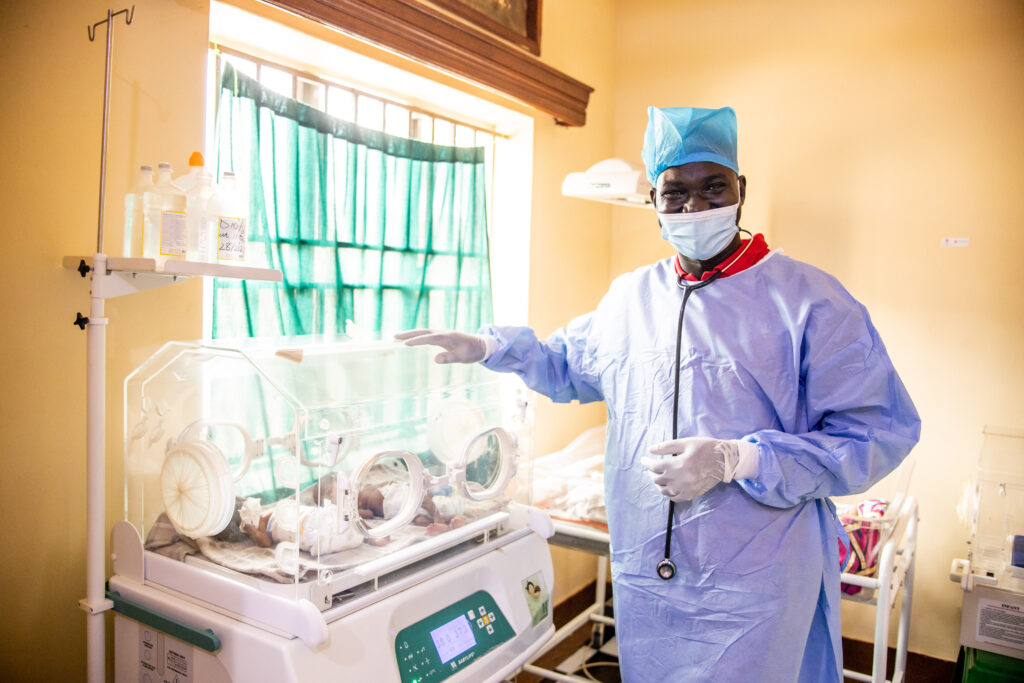 A doctor stands next to an incubator in a NICU unit