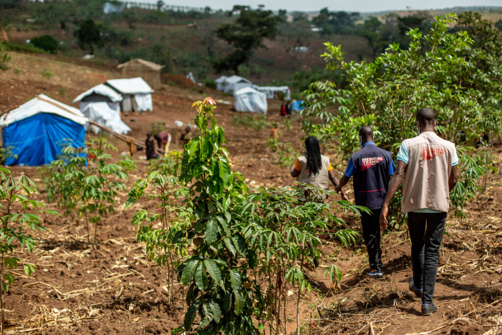 Three Medical Teams staff walking toward homes in a refugee settlement