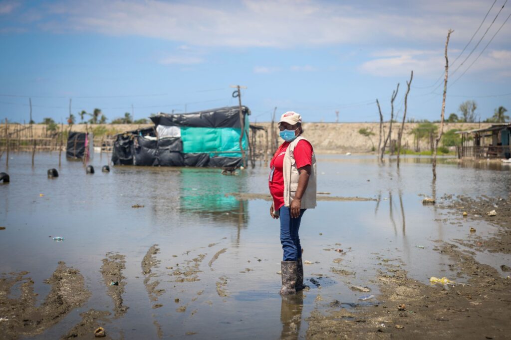 A woman in rain boots wades through over a foot of water from flooding in her community.