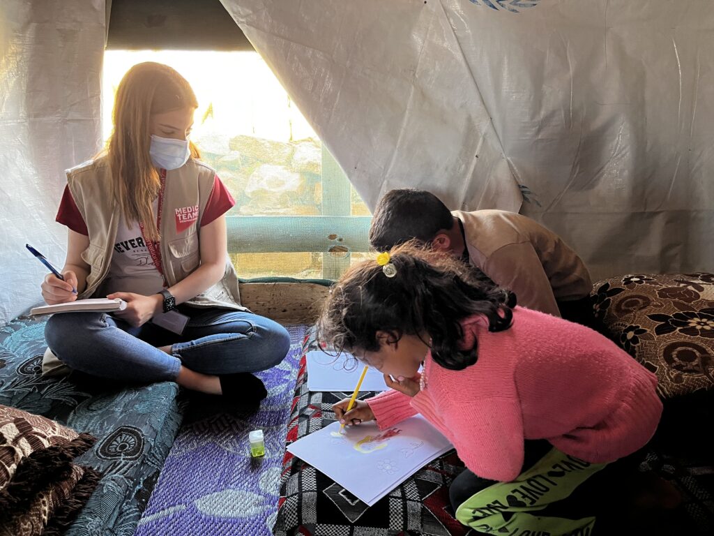 A woman sits in a tent with children who are drawing pictures.