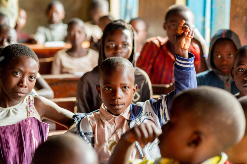 Thiery raises his hand in a classroom surrounded by other kids.