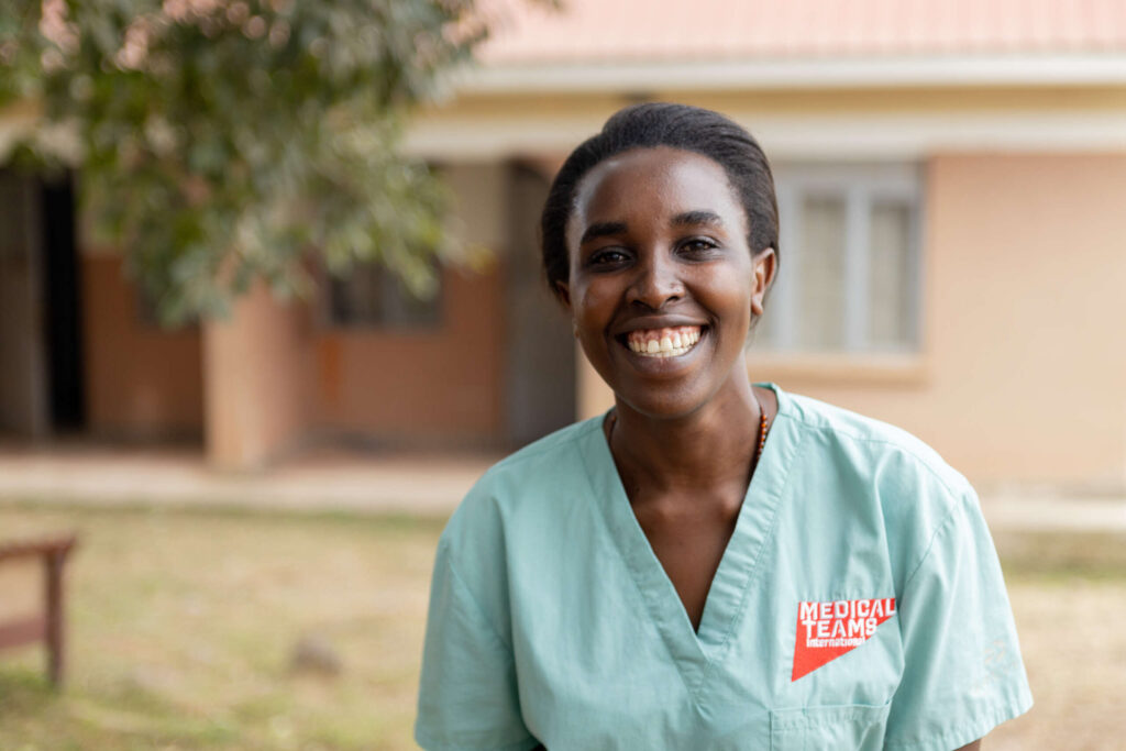 A woman smiles, standing in front of a building.