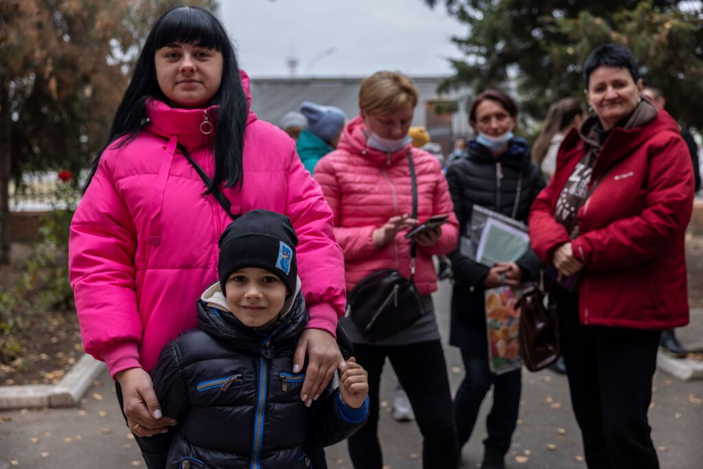 a woman and her young son pose for a photo while waiting in line