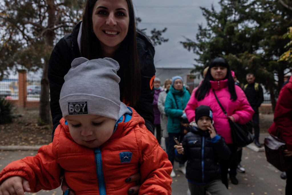 Ukraine photo: a woman smiles with her young son as they wait in a line of people