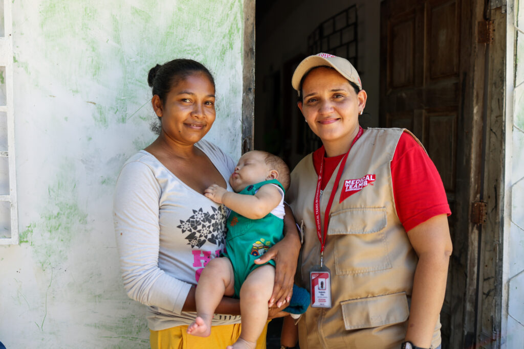 A mother and her baby pose with a Medical Teams staff person