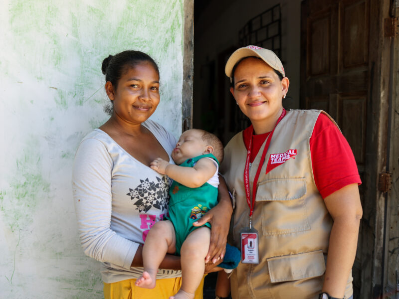 A mother and her baby pose with a Medical Teams staff person