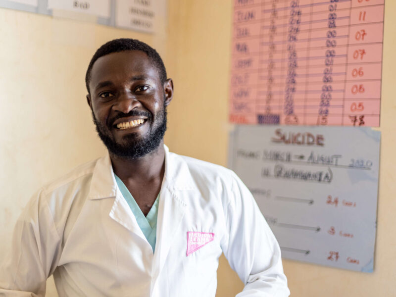 A Ugandan psychiatrist poses in his clinic with a wide smile.