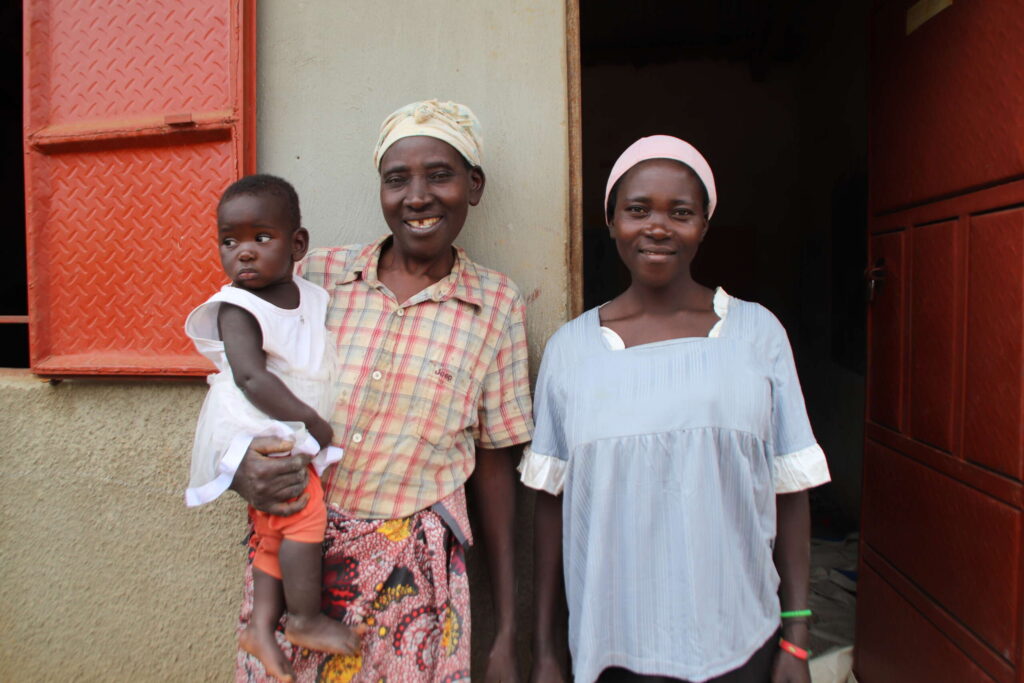 An older woman holds a child in her arms and stands next to another smiling woman.
