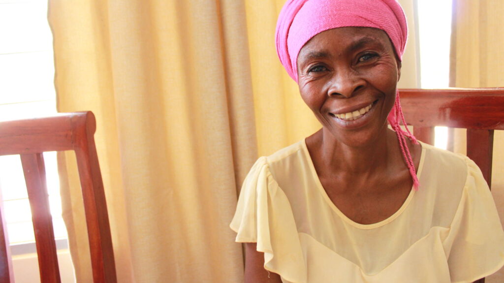 A woman in a pink hairwrap smiles into the camera.