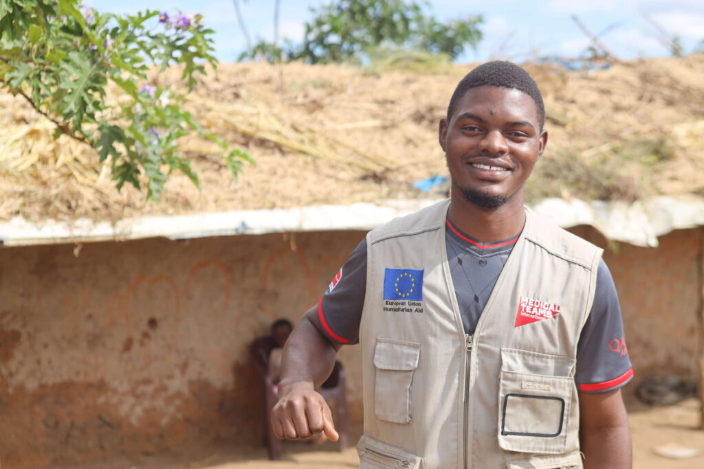 A man in a humanitarian aid worker vest smiles for the camera.