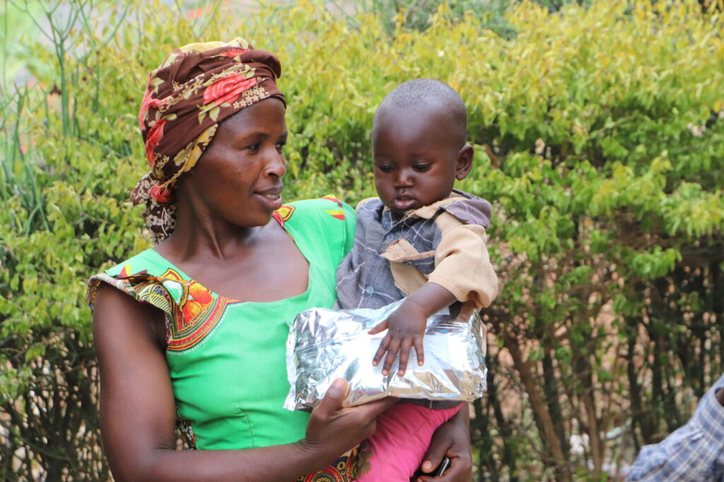 A woman holds a toddler with a pack of supplementary nutrition