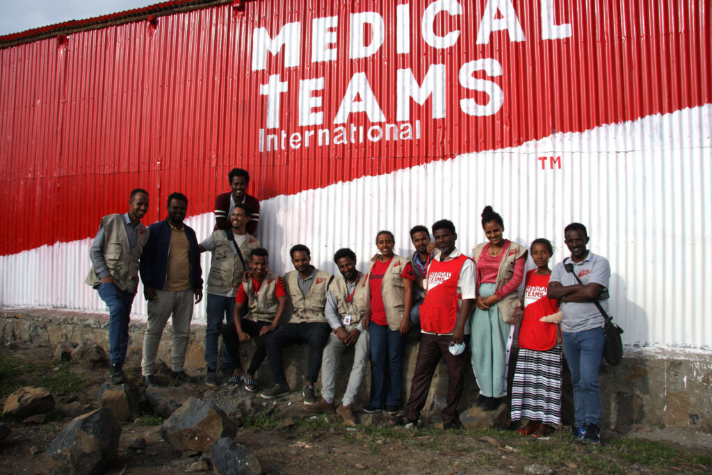 Group photo of staff and CHWs in front of the Medical Teams wall at the new clinic, 2022